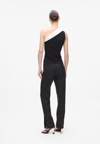 Black sleeveless top with an asymmetric white strap, paired with black trousers. Features a smooth texture and tailored fit.