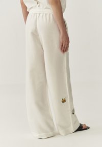 Witte linnen broek met wijde benen en een elastische tailleband, versierd met kleurrijke geborduurde accenten op het linkerpoot.