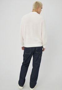 Pull en maille côtelée rose clair avec un col rond associé à un jean cargo bleu foncé, comportant plusieurs poches et des coutures contrastées.