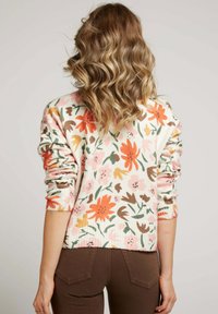 Pull en maille à motifs floraux de couleur rose clair, avec des fleurs orange, marron et vert. Texture côtelée avec des poignets et un ourlet roulés.