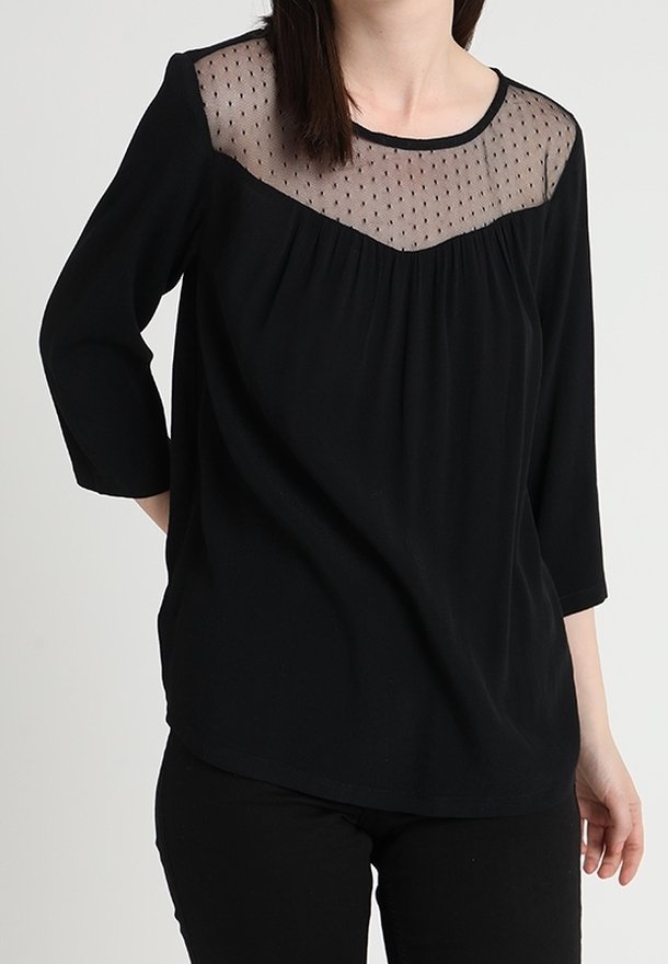Haut noir avec tissu transparent à pois sur le yoke, manches trois-quarts et corps souple et fluide. Encolure arrondie et détail plissé à l'avant.