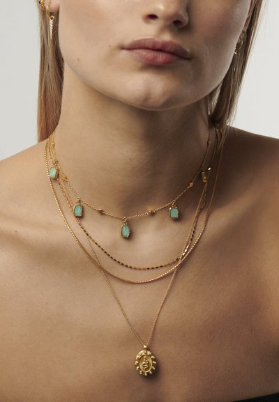 Coliere din aur cu straturi, prezentând accente de turcoaz, un pandantiv central cu detalii intricate și diferite texturi și lungimi ale lanțului.