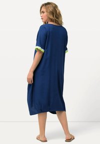 Marineblauwe jurk tot de knie met korte mouwen en groene en witte accenten. Gemaakt van lichtgewicht stof, met een ontspannen pasvorm en zijsplitten.