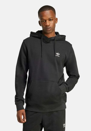 Melnā kapuce, kas izgatavota no mīksta auduma, ar kenguru kabatu un mazu baltu Adidas logotipu uz krūtīm. Iekļautas velkamo auklu siksnas kapuces daļā.