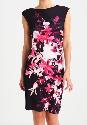 Abito nero senza maniche con stampa floreale brillante in rosa, bianco e viola, silhouette attillata, lunghezza al ginocchio, indossato da una persona in piedi.