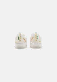 Fehér sneaker, bordás textúrával, kék és sárga részletekkel, húzófülekkel és dombornyomott logóval a sarkán. Könnyű kialakítás.