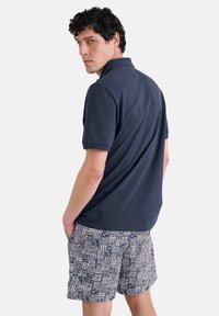 Námornícky polo tričko a kockované šortky v modrých a bielych odtieňoch s geometrickými vzormi. Mäkka textúra, s krátkymi rukávmi a golierikom.