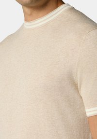 Béžové pletené tričko s krátkými rukávy a žebrovaným kulatým výstřihem se slušivými bílými pruhy. Měkká textura, přiléhavý střih.