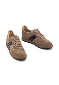 Beżowe zamszowe sneakersy z czarnym skórzanym paskiem i brązowymi akcentami. Sznurowana konstrukcja, okrągły nosek i teksturowana gumowa podeszwa.