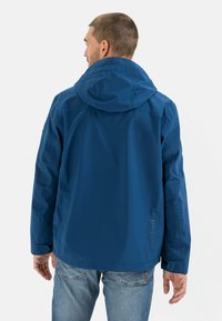 Blaue wasserdichte Jacke mit Kapuze, die eine glatte Textur, taillierte Bündchen und ein Logo nahe dem Saum aufweist. Die Rückansicht zeigt die Nahtdetails.