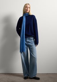 Marine brei sweater, lichtblauwe sjaal, wijde blauwe jeans en zwarte schoenen. Soepele texturen met een losse fit. Eenvoudig ontwerp, casual stijl.