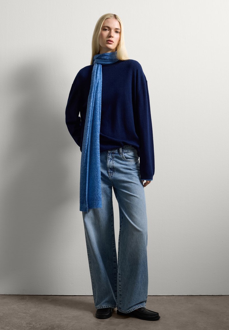 Marine brei sweater, lichtblauwe sjaal, wijde blauwe jeans en zwarte schoenen. Soepele texturen met een losse fit. Eenvoudig ontwerp, casual stijl.