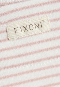 Biały materiał z jasnoróżowymi poziomymi paskami. Metka z napisem "FIXONI®" jest przyszyta beżową nicią wzdłuż dekoltu. Gładka tekstura.