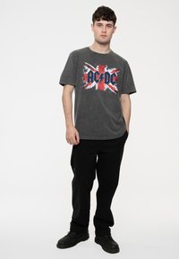 Gray cotton t-shirt featuring a distressed Union Jack design with "AC/DC" in bold navy lettering. Paired with black casual pants and shoes.