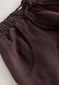 Pantaloni maro închis cu talie elastică și detaliu de buzunar lateral, prezentând textura țesăturii și cusăturile în prim-plan.