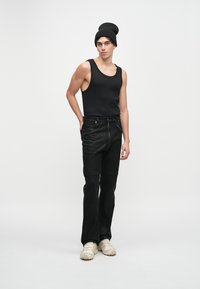 Crni top bez rukava, crne hlače sa zatvaračem i džepovima, stilizirane s crnom kapom i bež tenisicama. Jednostavan, prilagođeni dizajn.