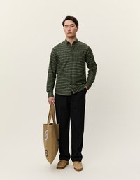 Zaļš pārbaudīts krekls, kas izgatavots no auduma, ar pogām un garām piedurknēm. Melni bikses, bežīgas apavus un brūnu tote somu ar uzlīmēm.