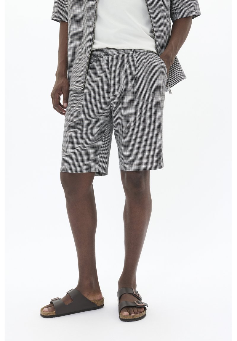 Shorts în carouri alb-negru dintr-un material elastic, cu un talie elastică și buzunare laterale. Purtați cu sandale închise la culoare.