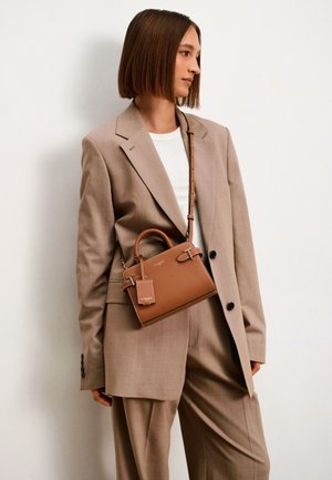 Brown leather handbag with a structured design, short handles, and a detachable shoulder strap. Features a small tag and subtle hardware accents.