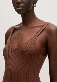 Bruine ribgebreide tanktop met dunne banden, voorzien van een V-hals en textuurstof, nauwsluitend op het lichaam.