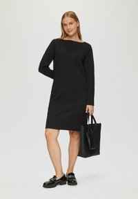 Abito nero a maniche lunghe con un motivo a spina di pesce testurizzato, taglio dritto, abbinato a scarpe nere lucide e una borsa a tracolla nera.