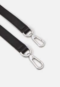 Černé kožené popruhy se stříbrnými kovovými otočnými karabinkami připojenými na každém konci na bílém pozadí.