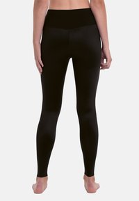 Schwarze Leggings aus strukturiertem Stoff mit hohem Bund, von hinten gezeigt. Das Design zeichnet sich durch eine enge Passform und glatte Oberfläche aus.