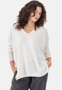 Pull léger crème à col en V, manches longues, poignets côtelés et fentes latérales ; texture douce et coupe décontractée.