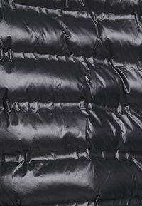 Primo piano di un giubbotto imbottito nero, con un design trapuntato caratterizzato da una texture in nylon lucido e liscio e cuciture orizzontali per l'isolamento.