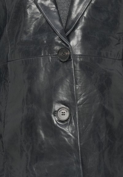 Blazer de couro preto com uma superfície texturizada, dois botões frontais e um colar estruturado. O tecido apresenta ligeiros vincos.