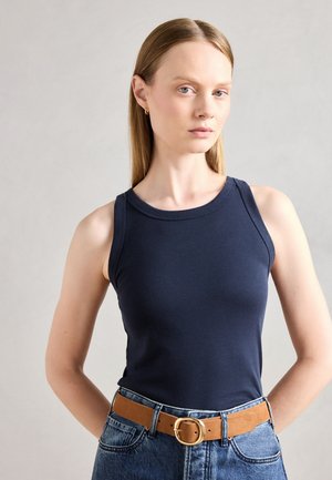Navy blue tank top made from a smooth fabric, featuring a round neckline and wide straps. Worn with high-waisted denim and a tan belt.