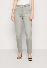 Szare jeansy z denimu o prostych nogawkach, z pięcioma kieszeniami, szlufkami na pasek i zapięciem na guzik. Noszone z czarnymi sandałami na obcasie.