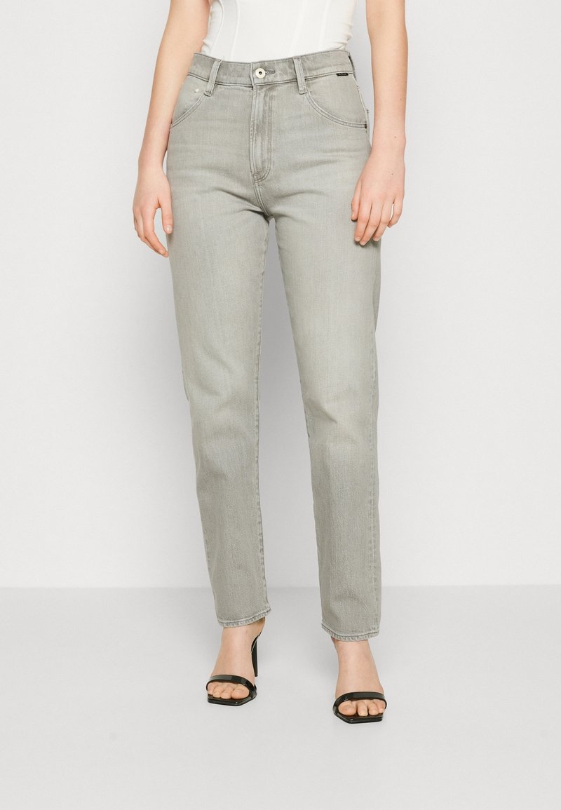 Szare jeansy z denimu o prostych nogawkach, z pięcioma kieszeniami, szlufkami na pasek i zapięciem na guzik. Noszone z czarnymi sandałami na obcasie.