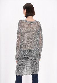 Langer, offener Strickcardigan in Schwarz und Weiß, mit lässiger Passform, langen Ärmeln und einem strukturierten Muster, das hinten bis zur Mitte des Oberschenkels reicht.