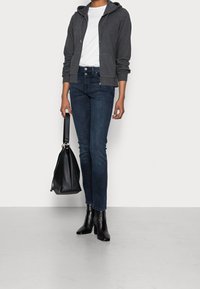 Grijze zip-up hoodie, witte T-shirt, donkere spijkerbroek, zwarte leren enkellaarzen en een zwarte leren handtas. Eenvoudige, casual outfit.