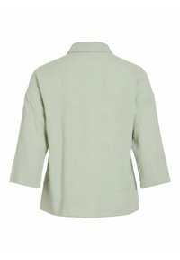 Blusa verde chiaro, con texture, dal collo a camicia e maniche a tre quarti. La vista posteriore mostra un tessuto liscio e una vestibilità rilassata.