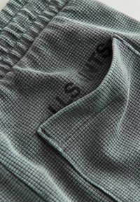 Detailný záber na sivú tkaninu s vafľovým vzorom a viditeľnou textúrou, s detailom elastického pásu.