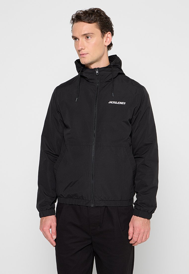 Veste légère noire avec capuche, fermeture éclair à l'avant, poignets et ourlet élastiques. Comprend un logo sur la poitrine et deux poches latérales.