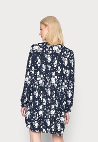 Vestido floral azul-marinho com padrões brancos, mangas longas, cintura franzida e um corte descontraído, confeccionado em tecido leve.