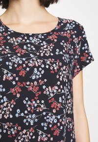 Krátký rukáv námorně modrý top s květinovým vzorem s malými červenými a světle modrými květinami, kulatým výstřihem a hladkou texturou tkaniny.