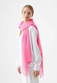 Écharpe rose en tissu léger, drapée librement autour du cou. Texture douce avec des bords frangés subtils qui rehaussent le design.