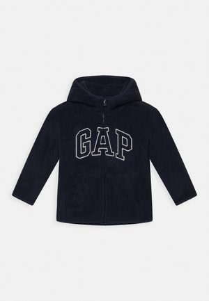 Sweat à capuche zippé en polaire bleu marine, avec une capuche, arborant le logo "GAP" en blanc. Deux poches latérales, manches longues, texture douce, design décontracté.