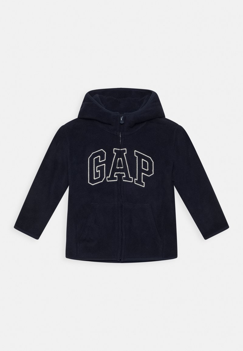 Sweat à capuche zippé en polaire bleu marine, avec une capuche, arborant le logo "GAP" en blanc. Deux poches latérales, manches longues, texture douce, design décontracté.