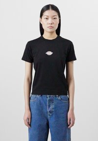 Black short-sleeve t-shirt with a small multicolored eye graphic at the chest, paired with loose blue denim jeans.