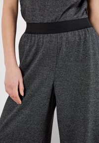 Zwart en grijs geruite wijde broek van een textuurstof, met een dikke zwarte elastische tailleband en geplooide details.
