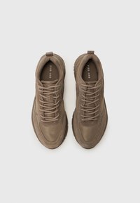 Brown athletic shoes with a mix of smooth and textured surfaces, round laces, and a cushioned sole. Features a logo on the insole.
