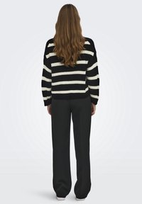 Pull en maille rayé noir et blanc avec une coupe décontractée, des manches surdimensionnées et un ourlet côtelé, associé à un pantalon noir ample.