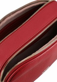 Borsa a tracolla in pelle rossa con texture, dotata di più scomparti con zip, hardware dorato e interno foderato, che mostra un dettagliato motivo di cucitura.
