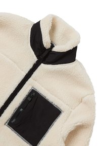 Giacca in pile crema con colletto alto, dettagli in nylon nero e una tasca con zip esterna. Presenta una texture morbida e materiali a contrasto.