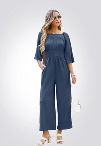 Navyblauwe jumpsuit met een vierkante halslijn, korte mouwen, een geraffineerde taille, wijde benen en zijzakken. Draag het met witte haksandalen.